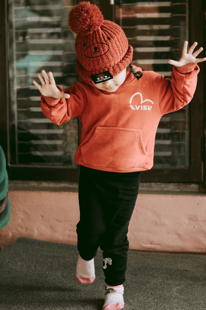 Adorable child in a red beanie and hoodie dancing happily indoors. Perfect lifestyle shot.