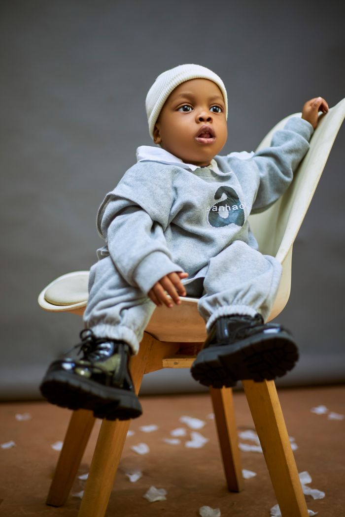 services-08 Cute baby in a casual gray outfit sitting on a modern chair with a neutral background.