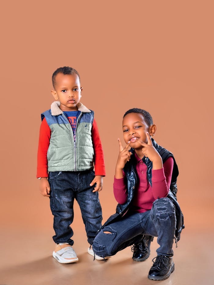 Two fashionable children posing against a brown backdrop, showcasing their trendy outfits.