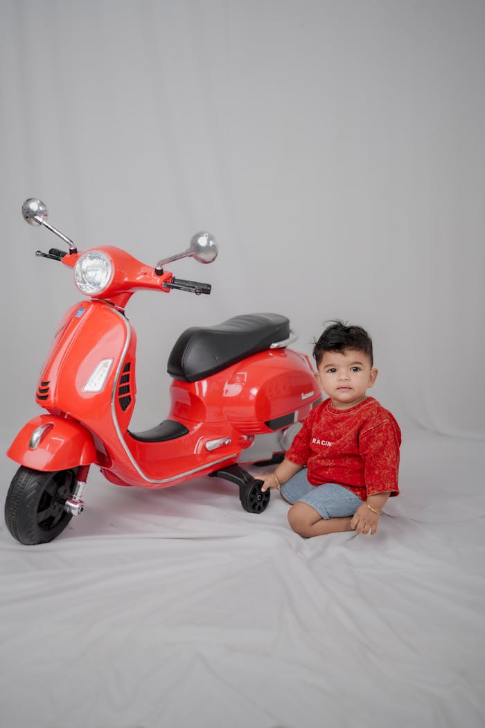 Charming portrait of a baby beside a vibrant red toy scooter.
