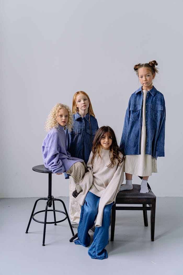 Four diverse children pose together on chairs in a minimalist studio setting.